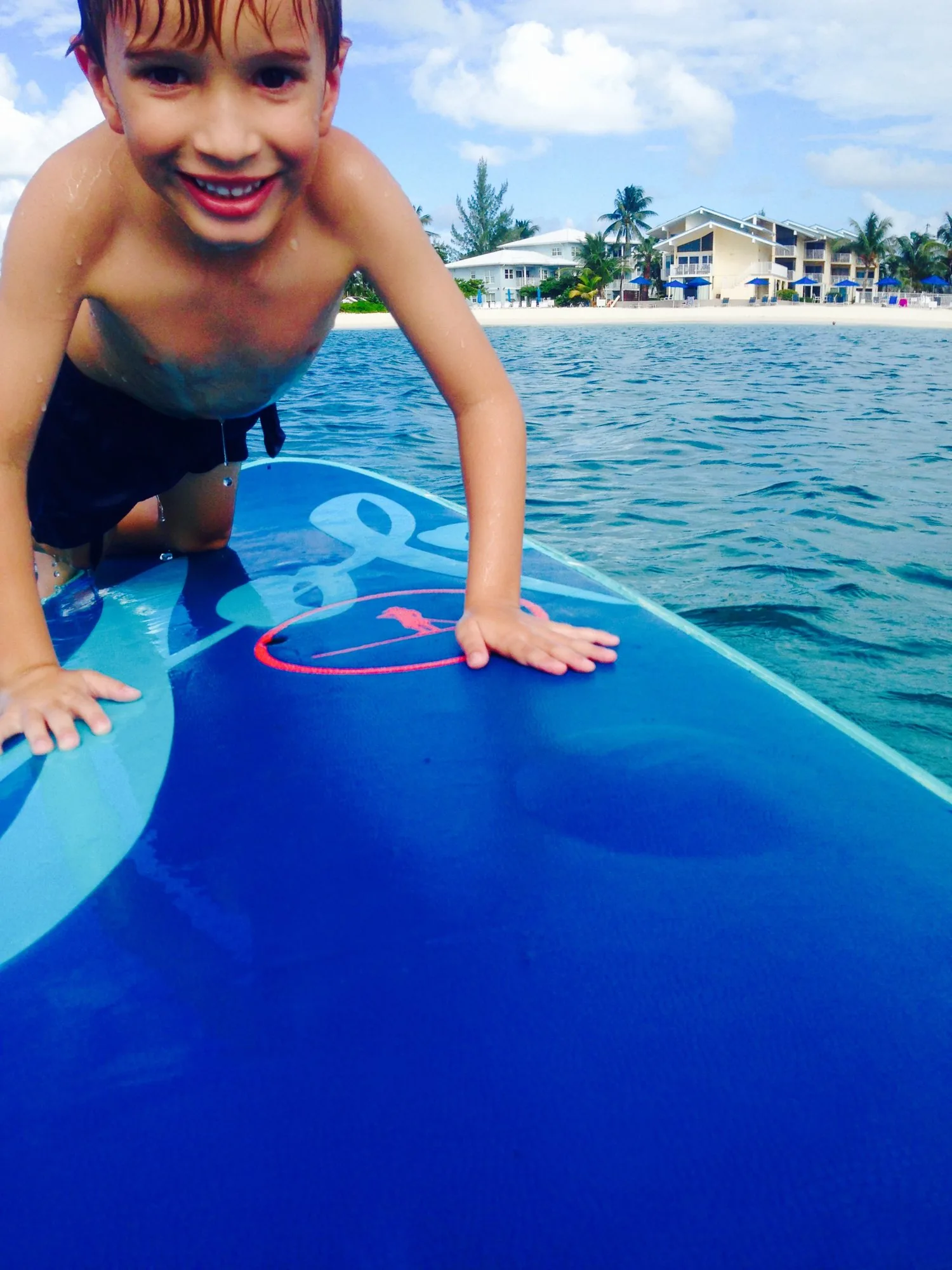 Smiling boy climbing onto a paddleboard off Seven Mile Beach