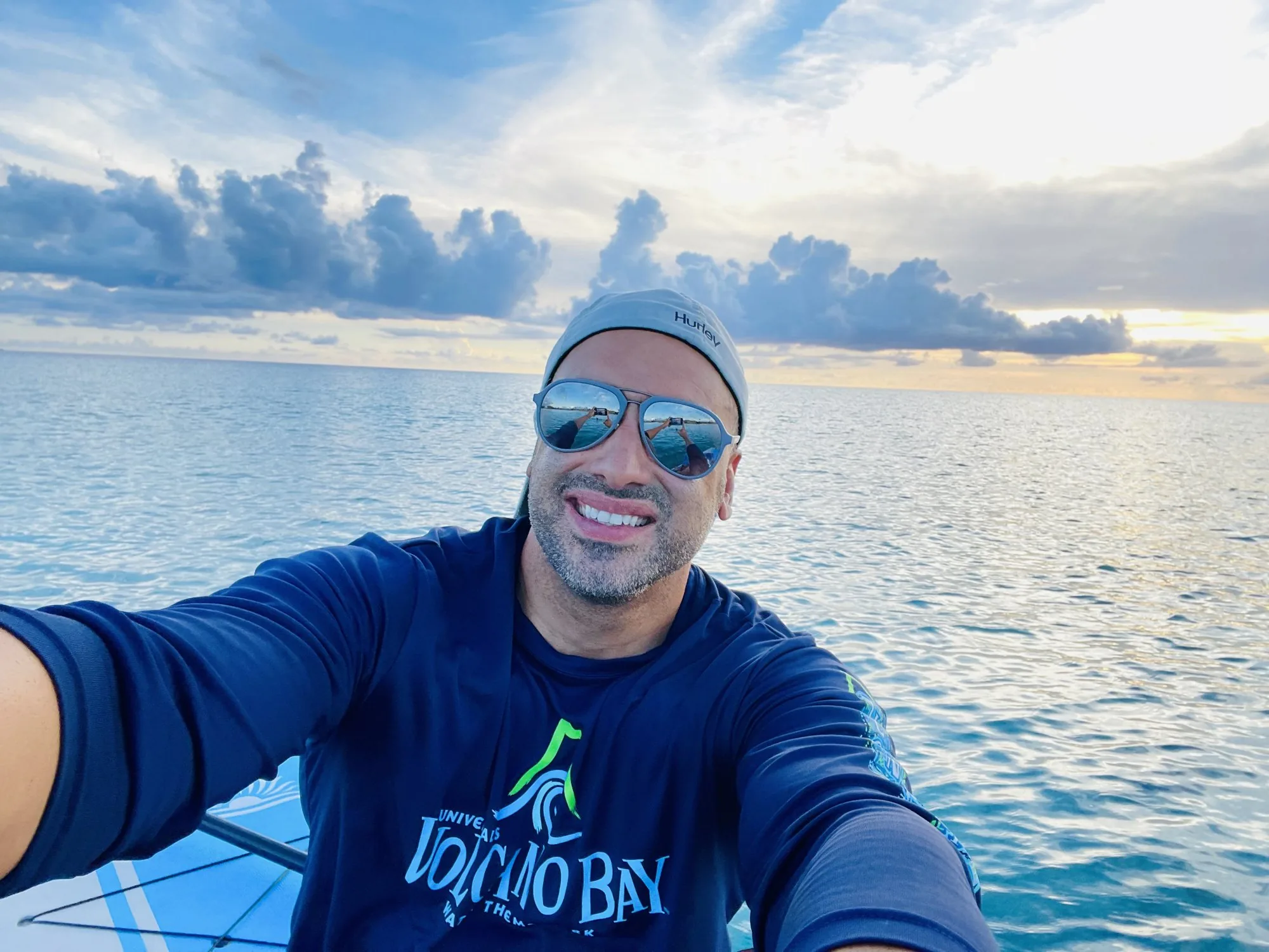 Smiling man in sunglasses taking a selfie on a paddleboard at sunset
